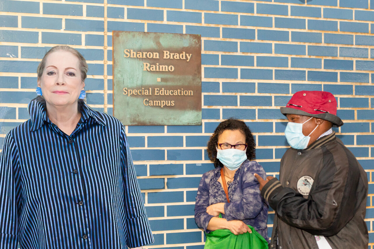 Sharon Brady Raimo standing next to the plaque at the entrance of building